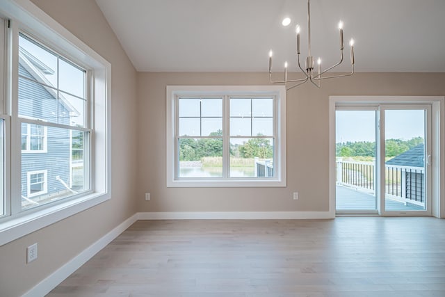 empty room featuring vaulted ceiling, plenty of natural light, an inviting chandelier, and light hardwood / wood-style floors