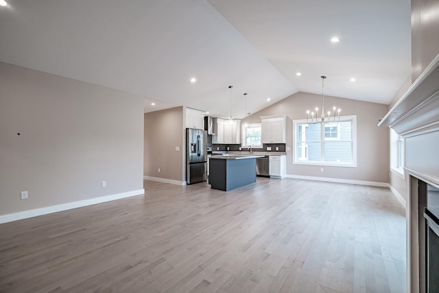 unfurnished living room with an inviting chandelier, lofted ceiling, sink, and light wood-type flooring