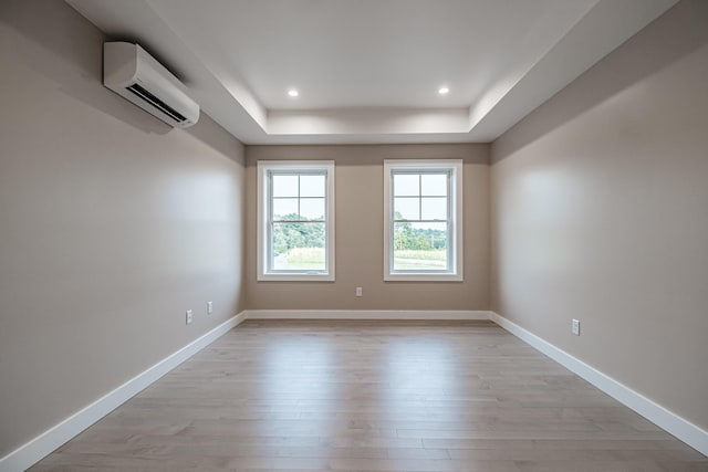 unfurnished room with a tray ceiling, a wall unit AC, and light hardwood / wood-style flooring