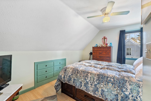 bedroom featuring lofted ceiling, a textured ceiling, light hardwood / wood-style flooring, and ceiling fan