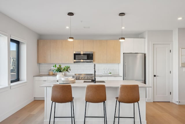 kitchen featuring light wood-style flooring, light countertops, appliances with stainless steel finishes, and a breakfast bar area