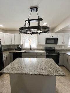 kitchen with white cabinetry, a center island, light stone counters, and black appliances