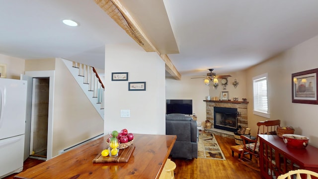 dining area featuring baseboard heating, ceiling fan, a fireplace, and hardwood / wood-style floors