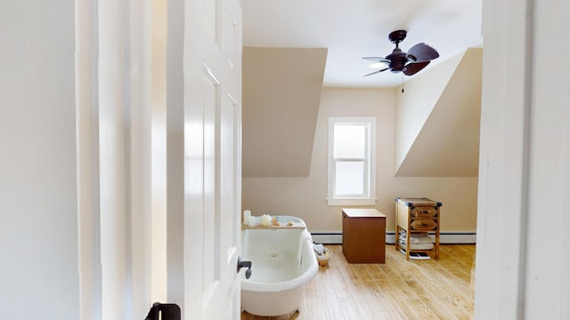 bathroom with ceiling fan, a bathing tub, hardwood / wood-style floors, and a baseboard heating unit