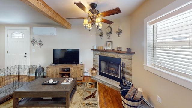 living room featuring a stone fireplace, a wall mounted air conditioner, beamed ceiling, wood-type flooring, and ceiling fan