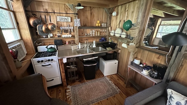 kitchen with a healthy amount of sunlight, white gas range, sink, and wooden walls