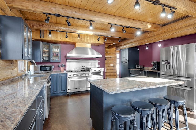 kitchen with stainless steel appliances, light stone countertops, a kitchen island, and wall chimney range hood