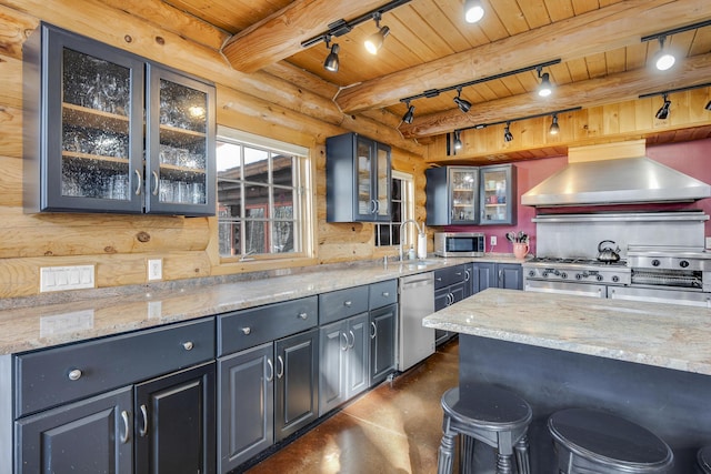 kitchen with appliances with stainless steel finishes, rustic walls, wood ceiling, light stone countertops, and wall chimney exhaust hood