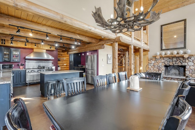 dining space with a fireplace, rail lighting, rustic walls, wooden ceiling, and beam ceiling