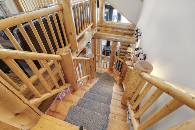 stairway featuring a towering ceiling, hardwood / wood-style floors, and rustic walls