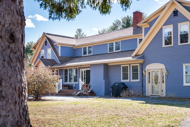 traditional-style home featuring a chimney, a front lawn, and a shingled roof