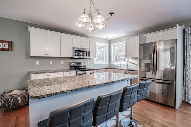 kitchen with appliances with stainless steel finishes, pendant lighting, white cabinets, and light wood-type flooring