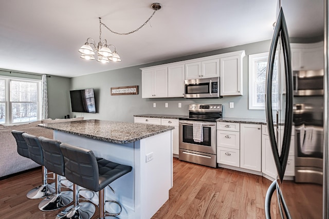 kitchen featuring dark stone countertops, white cabinets, a kitchen bar, light hardwood / wood-style floors, and stainless steel appliances