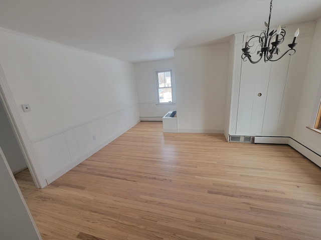 unfurnished dining area with light wood finished floors, a notable chandelier, baseboard heating, and a wainscoted wall