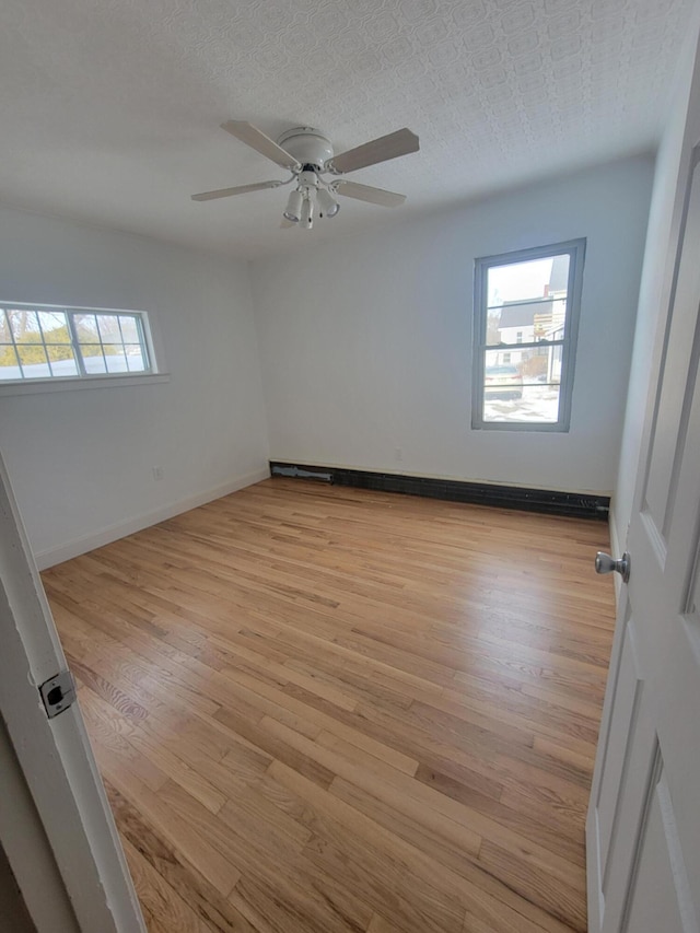 unfurnished room with light wood-style floors, a textured ceiling, baseboards, and a ceiling fan