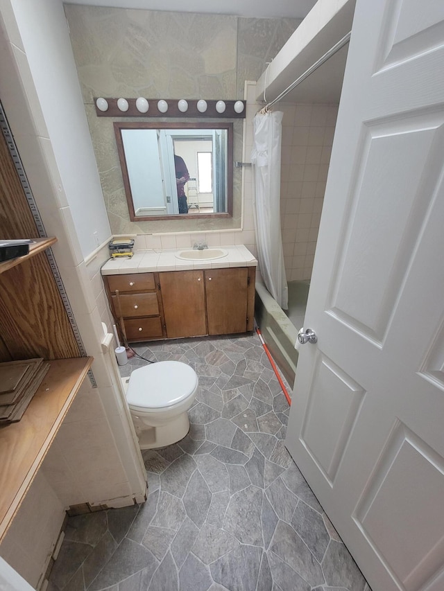 full bath featuring toilet, vanity, tile walls, stone finish floor, and shower / bath combo