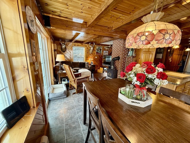 dining room featuring a wood stove, wooden ceiling, tile patterned floors, beamed ceiling, and wood walls