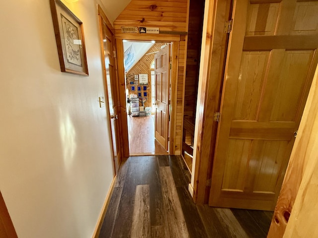 hallway featuring dark wood-type flooring, wooden walls, and vaulted ceiling