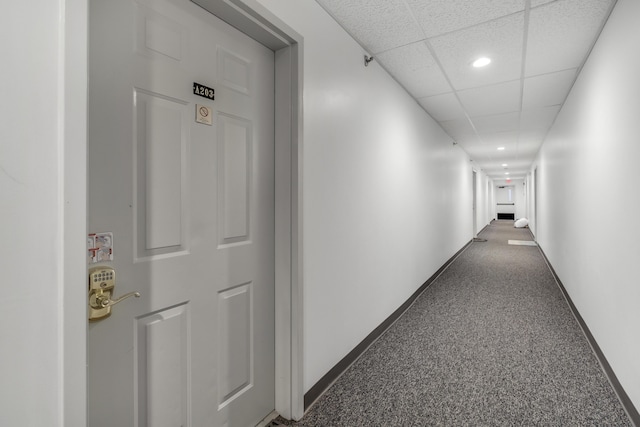 hallway with a drop ceiling and dark carpet