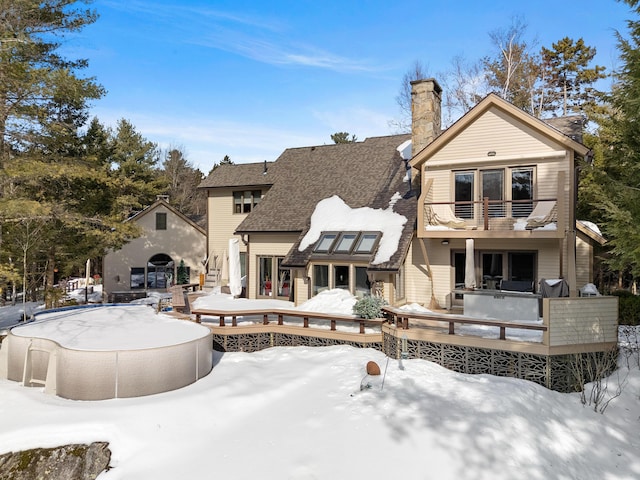 snow covered house featuring a deck, a pool, a chimney, and a balcony