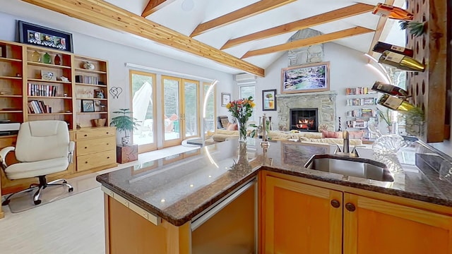 kitchen featuring dishwasher, open floor plan, dark stone countertops, vaulted ceiling with beams, and a fireplace