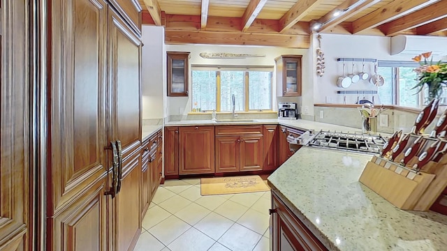 kitchen with light tile patterned floors, range, light stone counters, beamed ceiling, and a sink