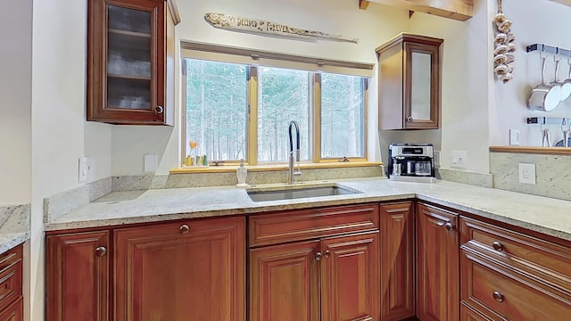 kitchen featuring light stone counters, glass insert cabinets, and a sink