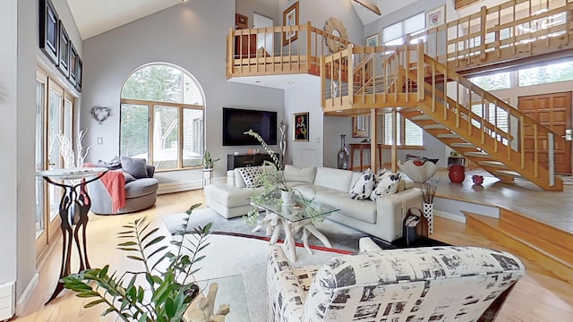 living area with a healthy amount of sunlight, stairs, high vaulted ceiling, and wood finished floors