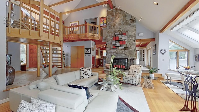 living area featuring beam ceiling, a stone fireplace, wood finished floors, high vaulted ceiling, and stairs