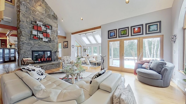 living area with high vaulted ceiling, a stone fireplace, and wood finished floors