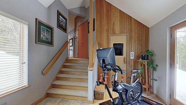 stairway featuring lofted ceiling, marble finish floor, wooden walls, and baseboards