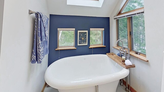 full bath featuring lofted ceiling with skylight, a soaking tub, and baseboards