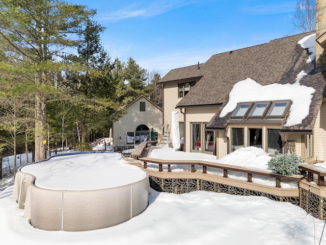 snow covered property with a swimming pool, roof with shingles, and a wooden deck