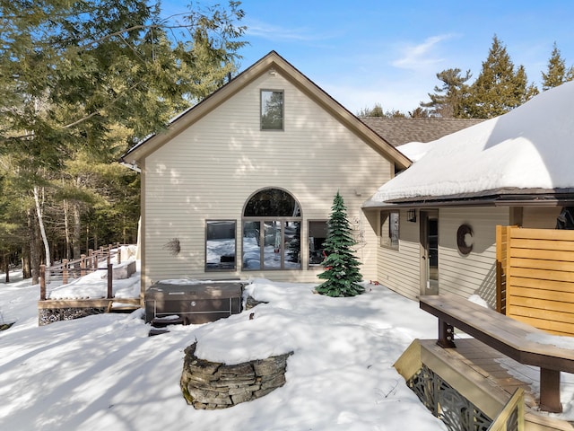 snow covered back of property with a hot tub and a patio