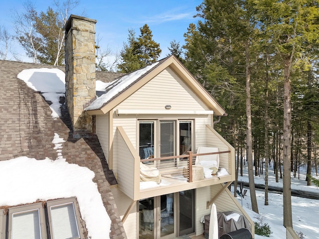 snow covered back of property with a shingled roof and a chimney