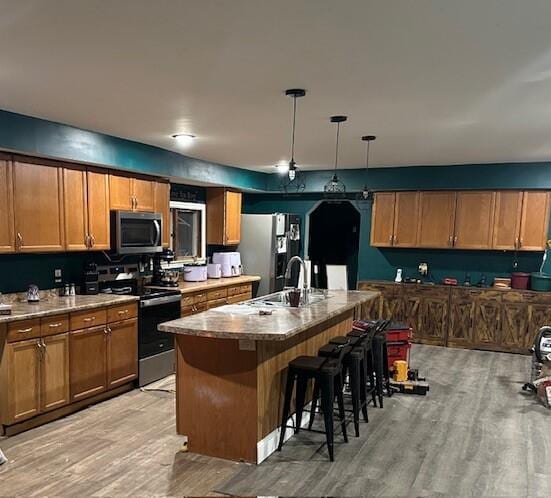 kitchen with appliances with stainless steel finishes, an island with sink, a kitchen breakfast bar, hanging light fixtures, and light hardwood / wood-style floors