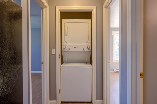 laundry area featuring a baseboard heating unit, laundry area, baseboards, stacked washer and dryer, and wood finished floors