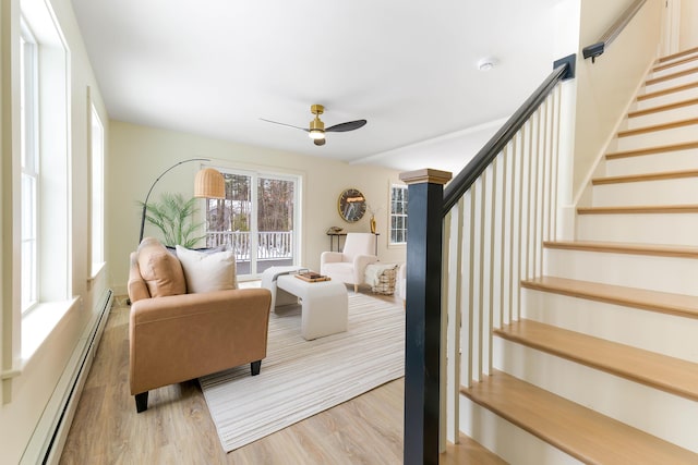 living area with a baseboard heating unit, stairway, wood finished floors, and a ceiling fan