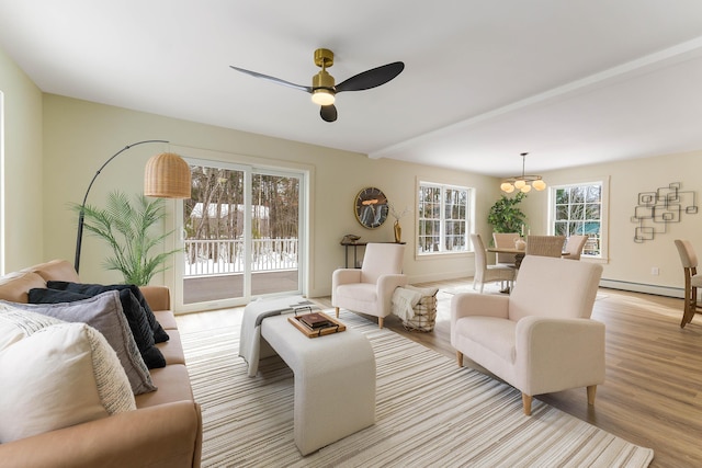 living area with a baseboard heating unit, ceiling fan with notable chandelier, and light wood-style flooring