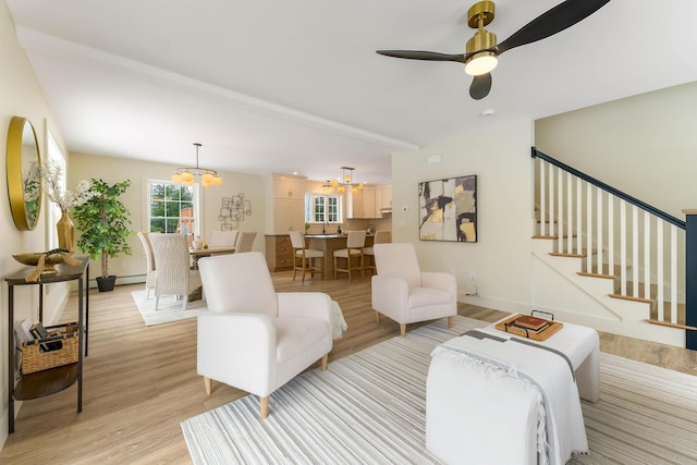 living room with stairs, light wood finished floors, a baseboard heating unit, baseboards, and ceiling fan with notable chandelier