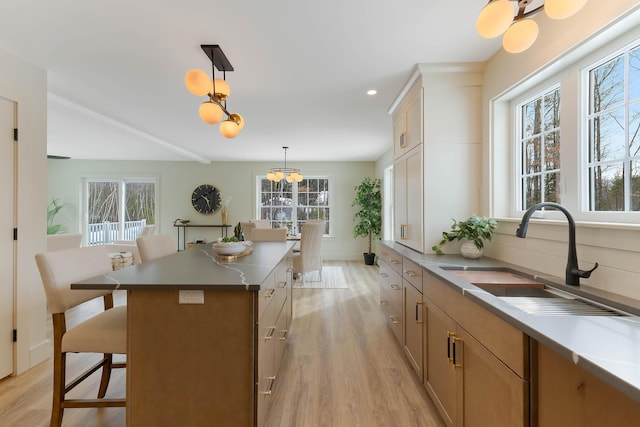 kitchen featuring light wood-style flooring, a breakfast bar, a sink, a center island, and pendant lighting