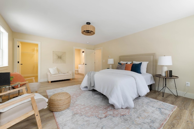 bedroom with connected bathroom, baseboards, and wood finished floors