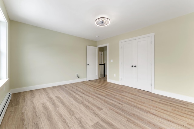 unfurnished bedroom featuring light wood-style floors, a baseboard radiator, baseboards, and a closet