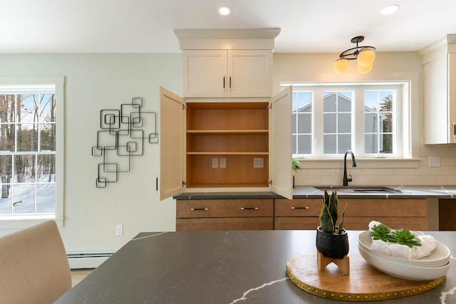 kitchen with a baseboard radiator, dark countertops, backsplash, white cabinets, and a sink