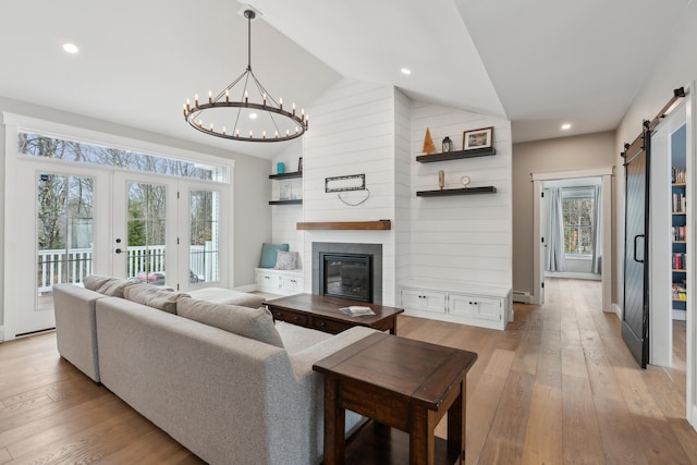 living room featuring light wood finished floors, a barn door, a fireplace, and vaulted ceiling