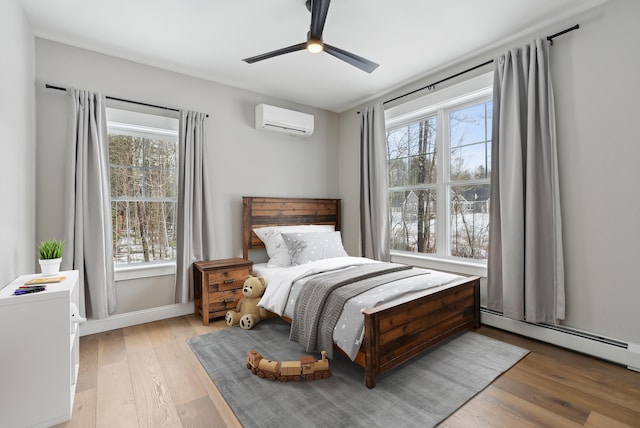 bedroom featuring an AC wall unit, light wood finished floors, multiple windows, and baseboard heating