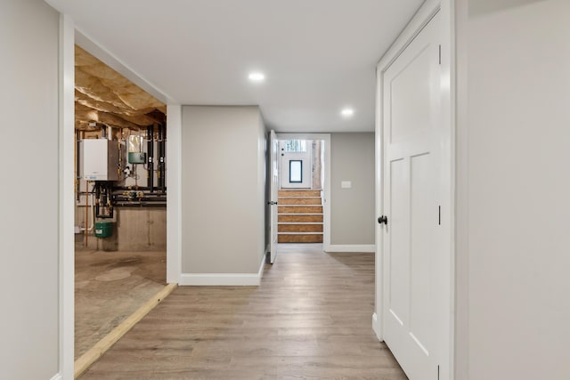 hallway featuring baseboards, stairway, wood finished floors, water heater, and recessed lighting