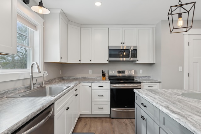 kitchen with appliances with stainless steel finishes, decorative light fixtures, light wood-type flooring, white cabinetry, and a sink