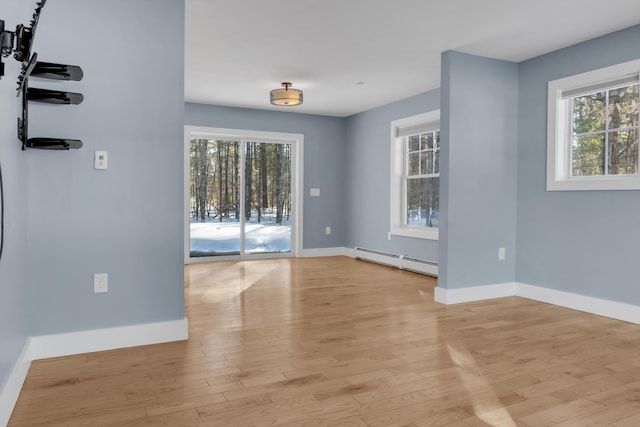 unfurnished room with baseboard heating, light hardwood / wood-style floors, and a healthy amount of sunlight