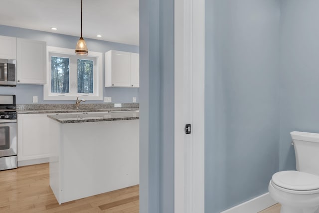 kitchen featuring white cabinets, light hardwood / wood-style flooring, stainless steel appliances, and decorative light fixtures